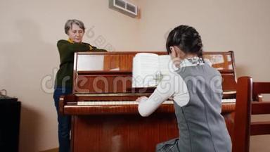 <strong>音乐</strong>课。 女孩弹钢琴，年长的<strong>老师</strong>站在钢琴附近。 从女孩的背后看游戏的画面
