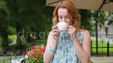 一个夏天咖啡馆里的<strong>女人</strong>正在<strong>喝茶</strong>，特写站着。 <strong>女人</strong>穿着裙子站在公园的背景上