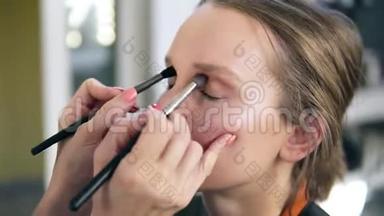 专业化妆师为年轻可爱的模特化妆.. 艺术家用两把刷子把眼影
