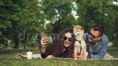 年轻女子正在公园里和男朋友和宠物狗躺在草地上自拍，可爱的<strong>动物</strong>在打喷嚏和