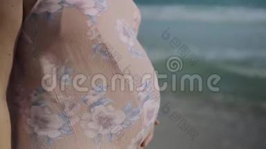 年轻的孕妇站在<strong>蓝色</strong>海洋附近的海滩上呼吸，靠近手和腹部。 暑假假期