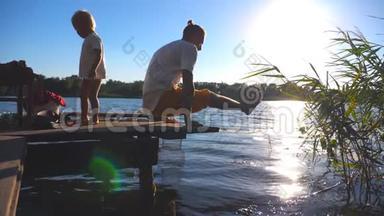 阳光明媚的夏日，年轻人在湖边的木制码头上练习瑜伽。 小孩和他爸爸