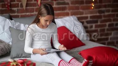 圣诞快乐的小女孩帕贾玛用圣诞老人送给她的数码平板电脑坐在卧室里，装饰着家