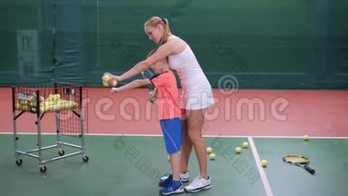 身着白色短裙的女教练正在教小男孩在室内球场玩耍。 职业网球