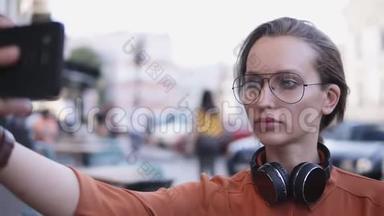 年轻的女人，白天<strong>化妆</strong>站在街上，用她的智能<strong>手机</strong>自拍。 模糊的街道