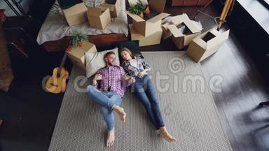 一对年轻夫妇躺在卧室的新房子的地板上，谈笑风生，牵手。 卡顿