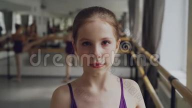 在宽敞的芭蕾课上，年轻女孩以化妆看镜头、微笑开始芭蕾舞蹈的肖像