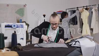 裁缝或时装设计师坐在工作室的工作场所，一边用大剪刀或剪刀剪布