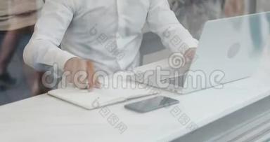 年轻的商人在看玻璃咖啡馆里的笔记本电脑时，在笔记本上写下商业信息。 慢动作