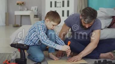严肃的小男孩专心致志地在<strong>父亲帮助</strong>他的时候用螺丝刀把木头碎片放好