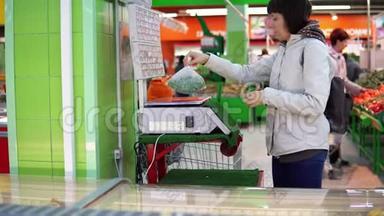 一个年轻的女人在商店里的电子秤上<strong>称重</strong>蔬菜。