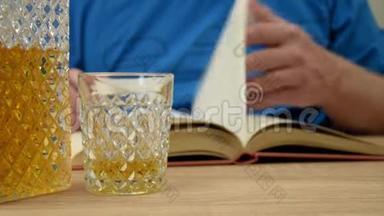 酒精饮料在水晶蜕膜。 一个人手里拿着一杯，<strong>倒了</strong>一杯威士忌饮料。 用眼镜打开书。
