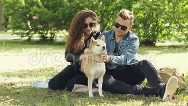 夫妻幸福的一对夫妻在公园里坐在<strong>草地上</strong>闲聊着他们的宠物石坝鱼<strong>小狗</strong>。 对话