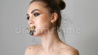 一个漂亮的年轻女孩模特的肖像，她的<strong>眼睛化妆</strong>时髦，嘴唇上有一只蝴蝶摆在面前
