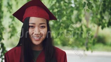 站在校园里，微笑着，身着长袍和灰泥板的亚洲女<strong>毕业生</strong>慢镜头画像