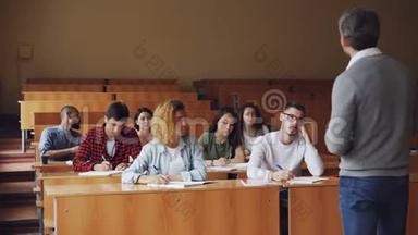 教师正在宽敞的大学报告厅与坐在课桌前的学生交谈，穿着便服的年轻人