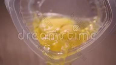 从杯子里倒入的生鸡蛋的特写。 库存录像。 含有蛋黄和蛋白质的生鸡蛋从塑料容器中扩散，