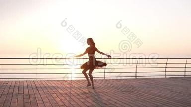穿着黑色芭蕾舞裙的芭蕾舞女芭蕾舞女演员，日出时在海洋或海上的堤岸上指着。 跳芭蕾舞，练习