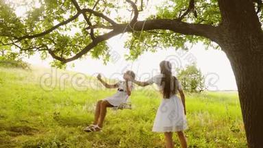 快乐的孩子们在一棵夏天的橡树下荡秋千，笑起来。 青春期的女孩在大自然中一起玩耍，微笑。