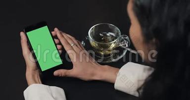 年轻的女商人使用带有绿色屏幕触摸板的smarthpone，并在咖啡馆打手势接近。 女孩拿着手机