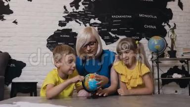 有两个孩子在地理课上看地球仪的老师。 可爱的男孩，女孩和老师用