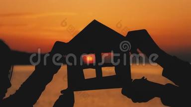 剪影一个用纸板做的小纸屋，在海上日落时用手握住。 效率及<strong>家居</strong>概念-