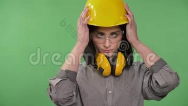 年轻漂亮的建筑女工，戴着耳机、眼镜和头盔，戴着头盔，严肃认真，戴着彩色钥匙