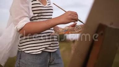 一位年轻的女艺术家在户外工作过程中的美丽景色。 油漆使用调色板和画架。 一阵风把她<strong>卷起</strong>来