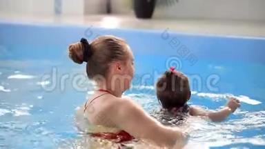 年轻的妈妈在游泳池里慢动作地和她的小女儿玩耍。 积极生活方式的体育家庭