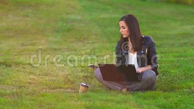 公园里的一个女孩在草坪上用笔记本电脑工作，电话<strong>铃</strong>响，接来电话。