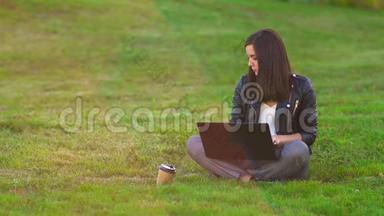 公园里的一个女孩在草坪上用笔记本电脑工作，电话铃响，接来电话。