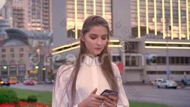 一个年轻漂亮、严肃的女孩正在夏季市中心日落时分在智能<strong>手机</strong>上<strong>输入</strong>信息