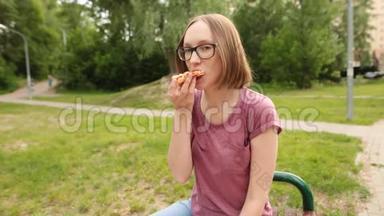 戴眼镜的滑稽时髦女孩坐在长凳上吃一片比萨饼。