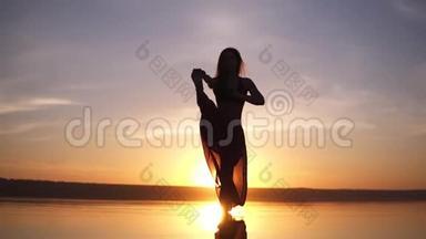 在美丽的夕阳下，在海上海岸练习瑜伽姿势的剪影瑜伽女人。 一个穿瑜伽裤的女人