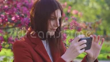 年轻迷人的红发女人在智能手机上拍摄樱花或樱花春花的背景自拍。