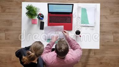 戴眼镜的年轻男子和拿着文件说话和指指点点的女人，<strong>上面</strong>有照片，桌子上有咖啡和<strong>笔记本</strong>电脑