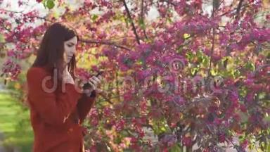 迷人的年轻红发女人在日落时在公园里使用手机。 背景樱花或樱花的春花