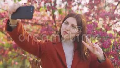 年轻迷人的红发女人在智能手机上拍摄樱花或樱花春花的背景自拍。