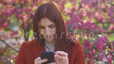 迷人的年轻红发女人在日落时在公园里使用手机。 背景樱花或樱花的春花
