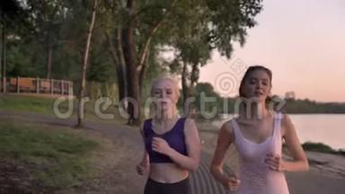 日落时分，两位梳着马尾辫的年轻漂亮的女跑步者在河边公园慢跑，减肥