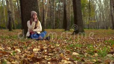 女孩独自<strong>坐在</strong>秋天的公园里，在一棵<strong>树下</strong>的地上。