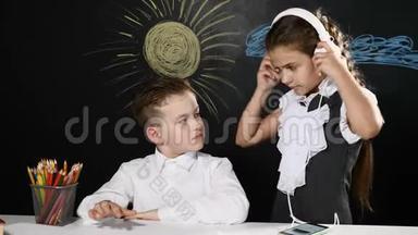<strong>学校理念</strong>。可爱的男孩和漂亮的女孩坐在书桌旁，身后是黑板。女学生给男孩戴上耳机