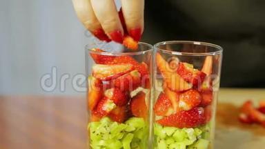 一个女人把碎<strong>奇异果</strong>片的成熟草莓放进玻璃杯里。