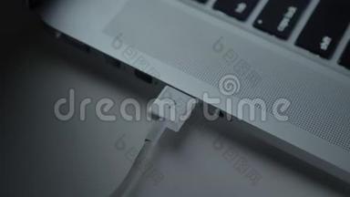 特写镜头的手快速插入白色USB电缆到笔记本电脑的黑桌背景。