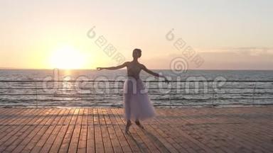 美丽的慢动作场景，年轻的芭蕾舞演员在室外的木制地板上缓慢地旋转。 海边，阳光普照
