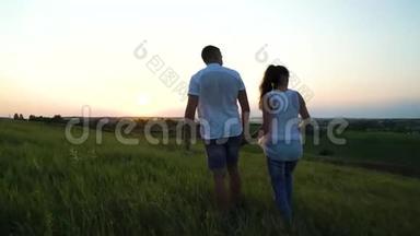 浪漫的年轻幸福的新婚夫妇在夕阳下的草地上散步