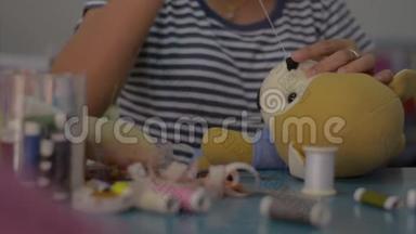 女人在家里的桌子上缝制和固定泰迪熊娃娃。