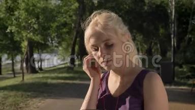 年轻的金发女郎戴着耳机，早上开始在河边的公园里跑步，面带微笑