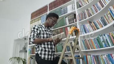 非洲男学生在大学图书馆里站在梯子上从书架上看书。