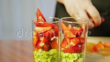 一个女人把碎奇异果片和成熟的草莓放进杯子里